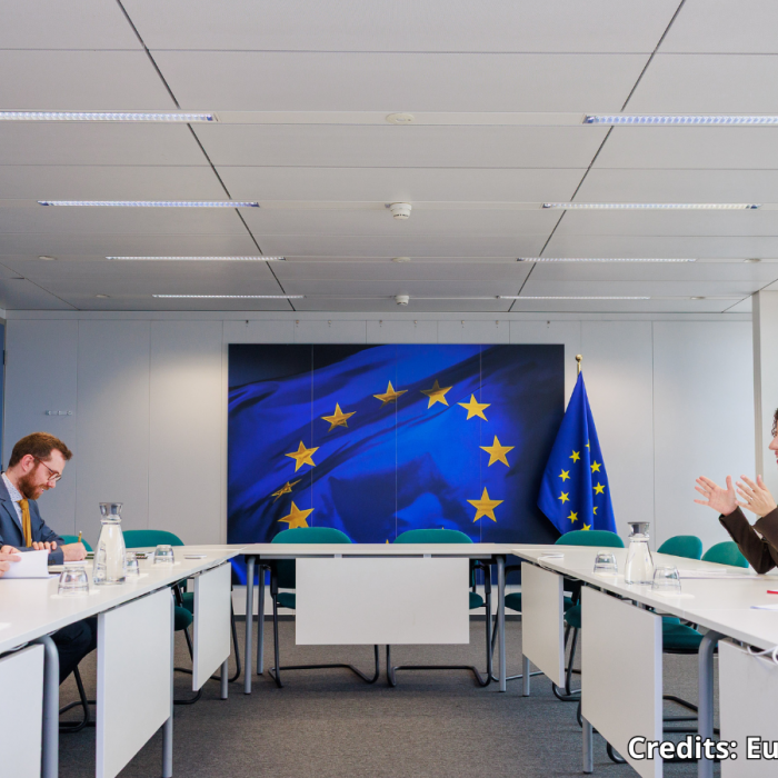 Στιγμιότυπο από τη συνάντηση των αντιπροσωπειών γύρω από τραπέζια τοποθετημένα σε σχήμα π, στο βάθος σημαία ΕΕ